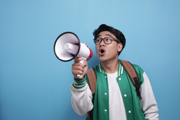 Young Asian male student wearing green baseball jacket shouting on megaphone