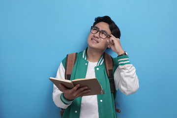 Male Asian student studying hard, reading a book against blue background
