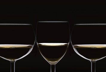 Closeup of three glasses of white wine silhouetted on black.