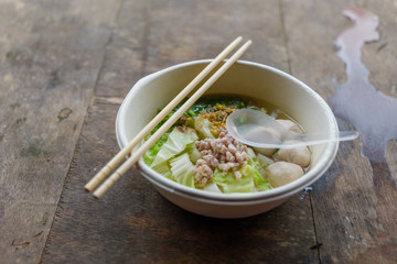 Rice noodle soup with pork balls, minced pork, cabbage and spring onion, serve in white foam bowl and wooden chopstick, on rough wooden. Eating noodle on outdoor street wood table.