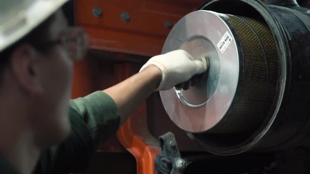 The mechanic changes the filter in the truck. He wears a helmet, a reflective vest, glasses and gloves. It's for safety.