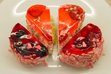 two cakes cut in half, one in the form of a heart, the second round with berry filling on a white plate close-up