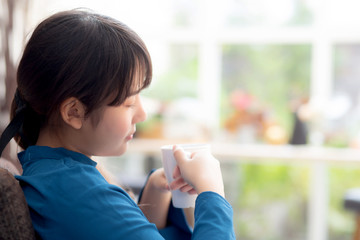 Back view asian woman sitting on chair with comfort and relaxing in living room at home drinking a cup of coffee or tea or beverage, lifestyle asia girl leisure healthy and wellness for satisfied.