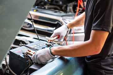 Close up of man hand charging a car battery using electricity trough jumper cables.