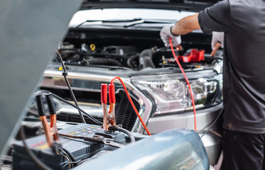Close up of man hand charging a car battery using electricity trough jumper cables. Selective focus at trough jumper head.