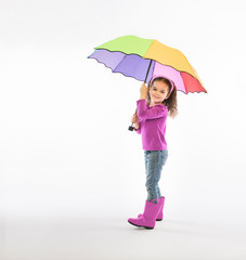 Smiling girl in matching pink shirt and rain boots holding rainbow umbrella on white background