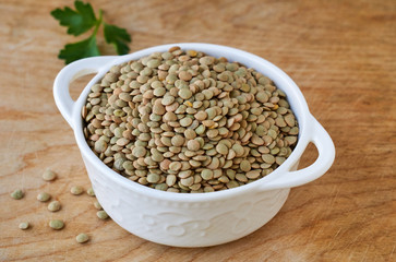 Raw green lentils in a white bowl on a wooden background 