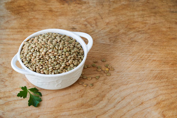 Raw green lentils in a white bowl on a wooden background 