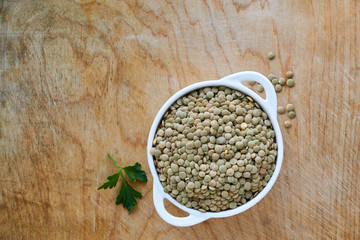 Raw green lentils in a white bowl on a wooden background 