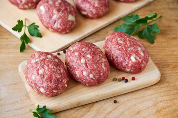 Raw minced meat cutlets on a wooden cutting board