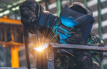 Welder is welding metal part in car factory