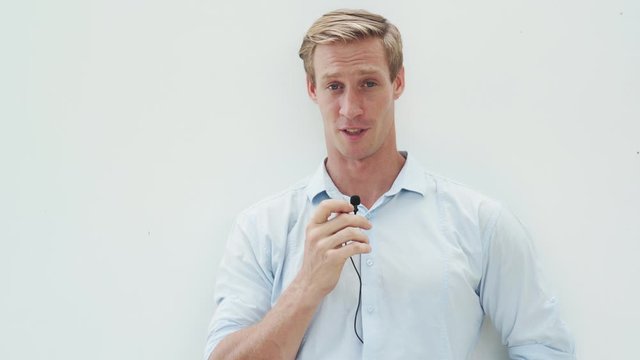 Portrait of young man speaks into microphone, looks at camera and smiles, white background