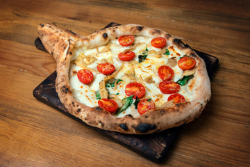 Freshly baked pizza with cheese, sauce, tomato and basil on a wooden table
