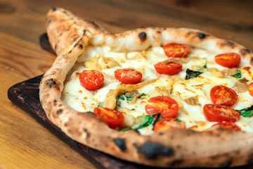 Freshly baked pizza with cheese, sauce, basil and tomato on a wooden table close up