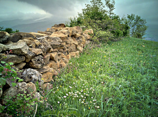 Stone fence in the plain in spring. Stone wall with a great cloudy sky in the beackground. Beautiful green meadow with a old Stone wall.