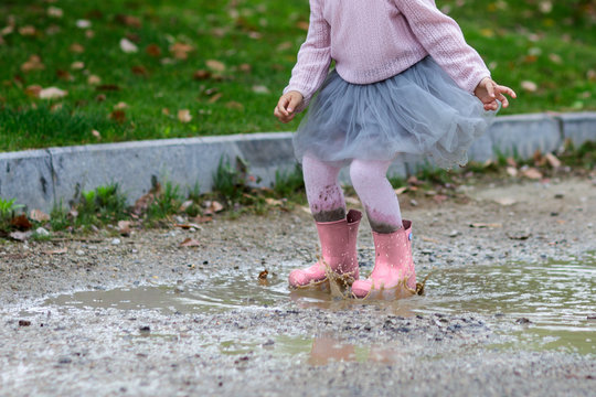 Feet of child in pink rubber boots jumping over a puddle in the rain