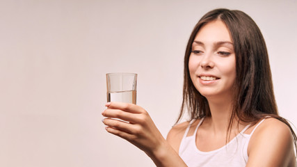 Young beatiful girl hold water glass. Hydrate female face. Happy women indoors. Morning routine. Pretty portrait