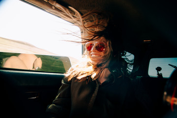 redhead girl sitting on back seat of a car and wind waving her hair