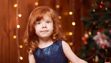 Christmas happy girl. Luxury attractive red hair child. Xmas miracle. Green tree, lights, bokeh
