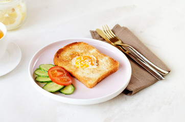 Brunch - an egg with sesame seeds on toast, fresh cucumber and tomato. A cup of tea with lemon. In the background is a can of sliced lemon with sugar. Cutlery lie on a textile napkin.