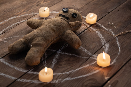 Voodoo doll on a wooden background with dramatic lighting and candles. The concept of witchcraft and black art and the occult. Burlap doll on the background of a drawn star. Stuck pins in the doll.