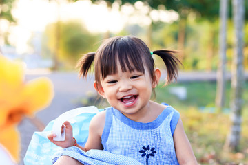 Portrait image of 1-2 years old baby. Happy Asian child girl smiling and relaxing at the garden park. Pretty girl wearing a blue dress. Summer season. Kids and travel concept.