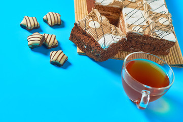 Sliced checkered rectangular cake on bamboo mat near full glass cup of tea and candies lies on blue table on party. Celebration concept. Space for text