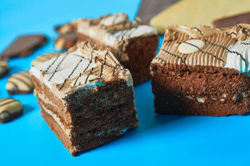 Sliced checkered rectangular cake near chocolate bar and candies lies on blue table on party. Celebration concept. Close-up