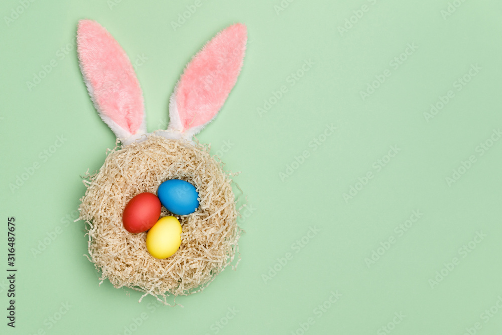 Poster nest with three easter eggs and bunny ears on a mint background. top view. copy space