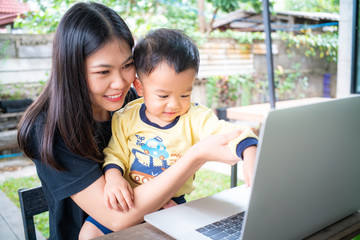 Smart young asian mom hold baby boy use laptop computer in cafe