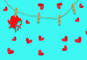 The Valentine's day concept.The red cupid shaped card attached to a wooden clip Hanging with hemp rope on blue background.Valentine's Day background