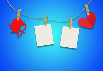 Valentine's day concept.Red cupid shaped card attached to a wooden clip Hanging with hemp rope on blue background.Valentine's Day background