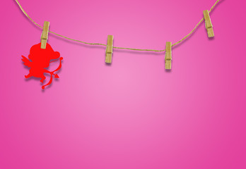 Valentine's day concept.Red cupid shaped card attached to a wooden clip Hanging with hemp rope on pink background.Valentine's Day background