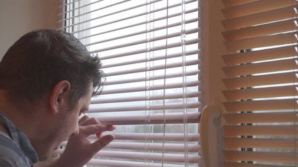curious man looks out the window through the blinds