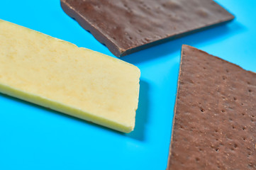 Scattered three various whole porous chocolate bars lies on blue table on kitchen. Close-up