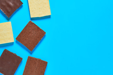 Scattered pieces of various whole porous chocolate bars lies on blue table on kitchen. Space for text. Top view