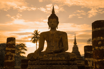 Obraz premium Ancient sculpture of a sitting Buddha close-up on a background of a sunset sky. Suchotai. Thailand