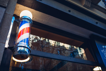 Barber's pole on a barbershop wall in the evening on a street of Barcelona, Spain