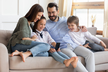 Overjoyed family with kids relax on sofa with smartphone