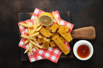 Fish and chips on a rustic wooden serving board, top view on a dark brown metal background