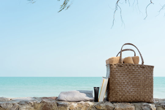 Weaving bag or Basket with towel, bottle of sun screen or sunscreen lotion, swimming robe and book next to a sea beach, summer travel concept for a rest in vacation time with copy space.