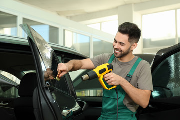Worker tinting car window with heat gun in workshop