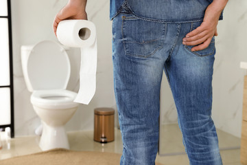 Man with toilet paper suffering from hemorrhoid in rest room, closeup