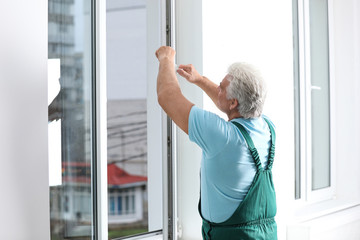 Mature construction worker repairing plastic window indoors