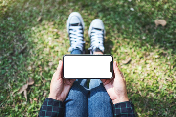 Top view mockup image of a woman holding black mobile phone with blank white screen while sitting...