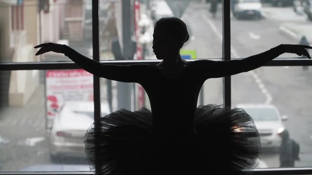Silhouette of a ballerina on a background of the city a beautifully moving dance. In a black tutu and Pointe shoes. The image of the black Swan from the ballet. Slow motion