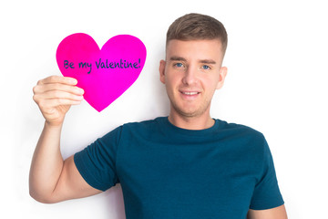Happy handsome guy, boy holding red valentine card in the shape of a heart with text Be my Valentine for Saint Valentineâ€™s Day. Young nice man smiling isolated on white background.