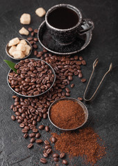 Cup of fresh raw organic coffee with beans and ground powder with cane sugar cubes with coffee tree leaf on black background. Top view