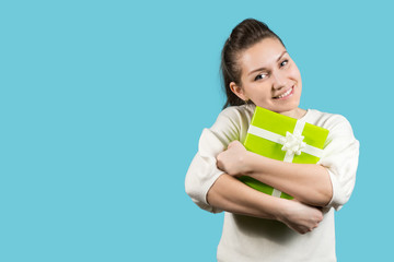 Young smiling girl presses a bright green gift against a blue background