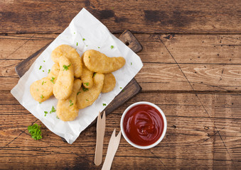 Buttered chicken nuggets on chopping board with wooden forks and ketchup on wooden background. Top view.